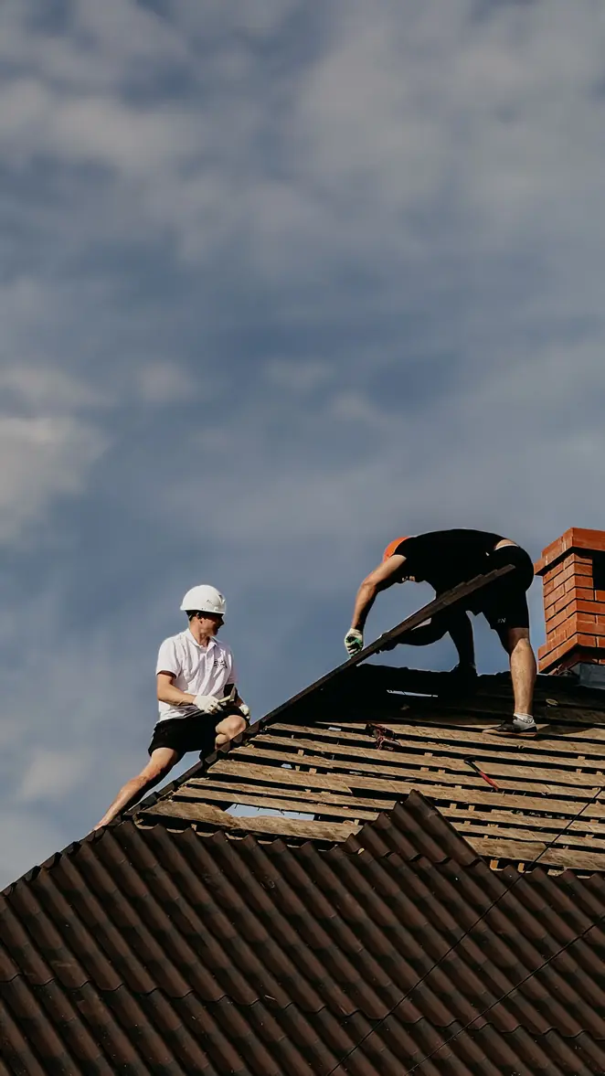 Deux couvreurs travaillant près du faîtage d'une toiture, vus en contre-plongée