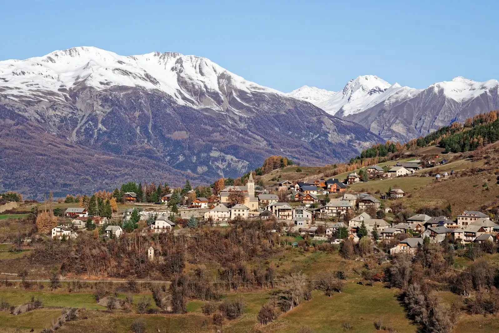 Village de montagne accroché à un versant, sommets enneigés en arrière-plan