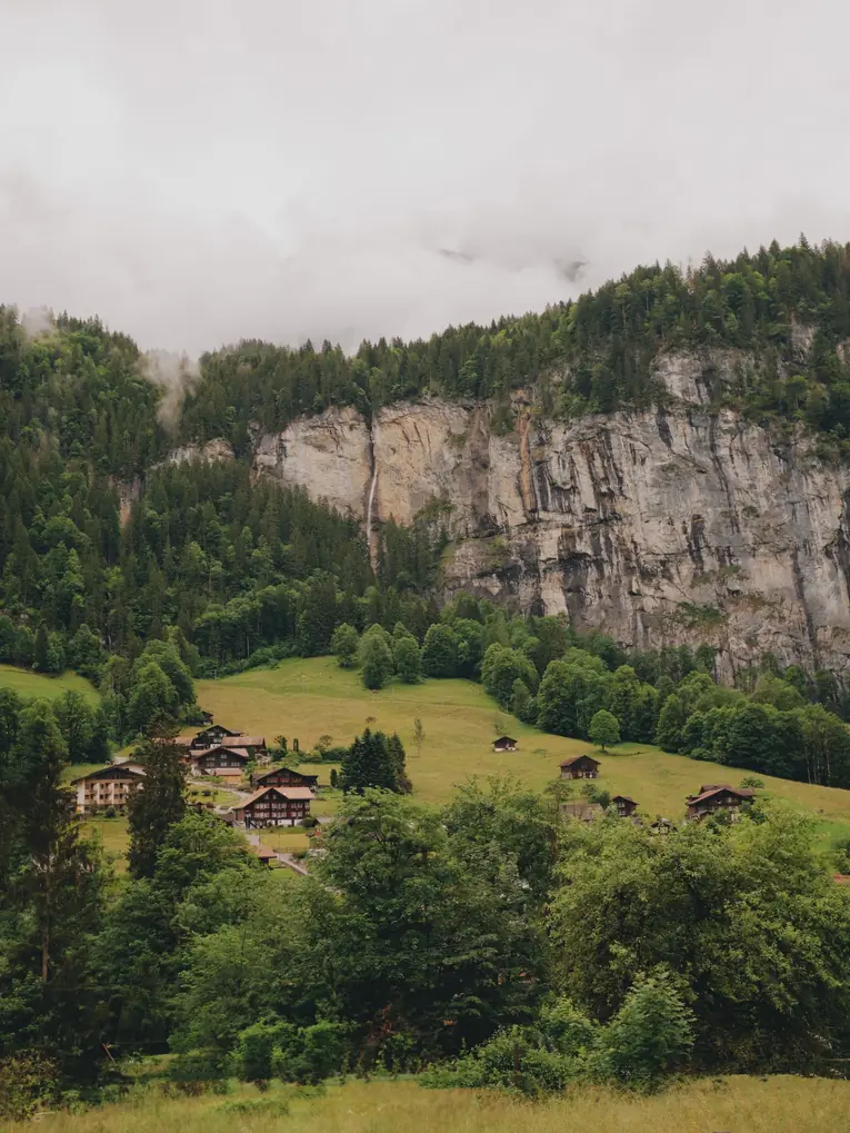 Hameau de montagne au pied d'une falaise, prairies et forêt